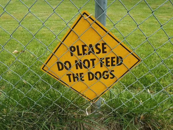 Yellow please do not feed the dogs sign on metal fence — ストック写真