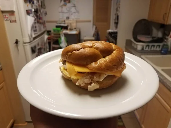 Σάντουιτς με αυγό, μπέικον και τυρί σε λευκό πιάτο στην κουζίνα — Φωτογραφία Αρχείου