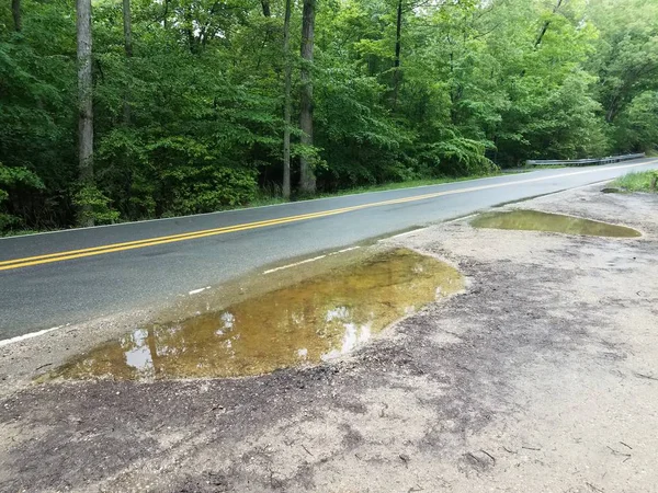 asphalt road and side of road with large water puddles