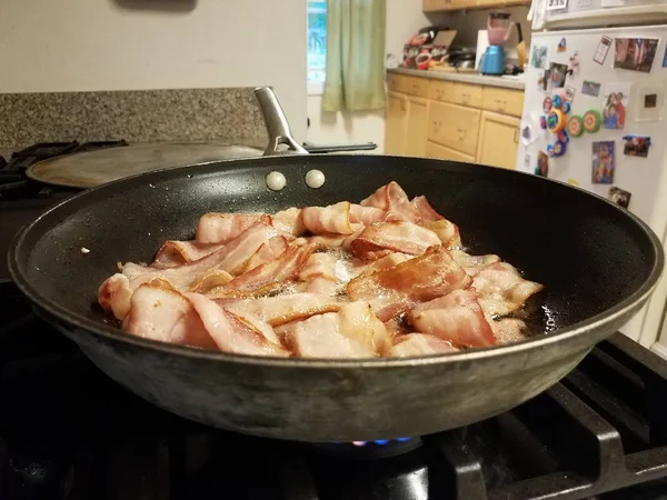 Bacon cooking in frying pan or skillet on stove in kitchen — Stock Photo, Image