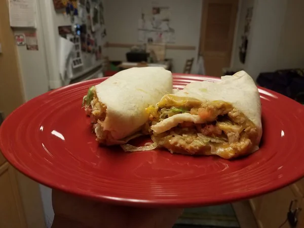 Kırmızı plaka üzerinde mutfakta tavuk ve peynir ile el tutarak tortilla — Stok fotoğraf