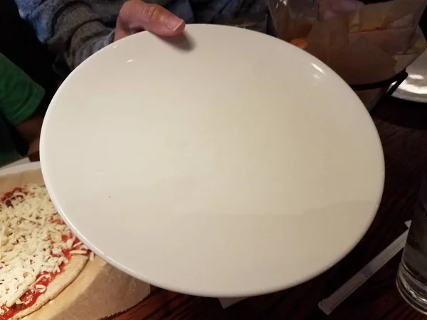 Ženy ruka drží prázdný bílý talíř v blízkosti pizzy — Stock fotografie