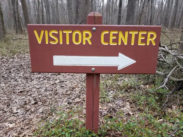 Signo de centro de visitantes marrón o rojo con flecha blanca derecha y árboles en el bosque —  Fotos de Stock