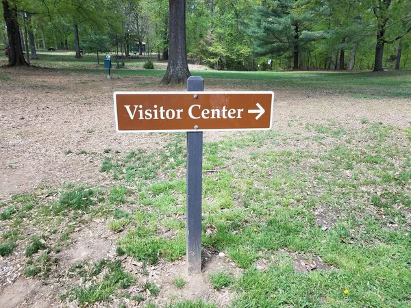brown visitor center sign with white right arrow and grass