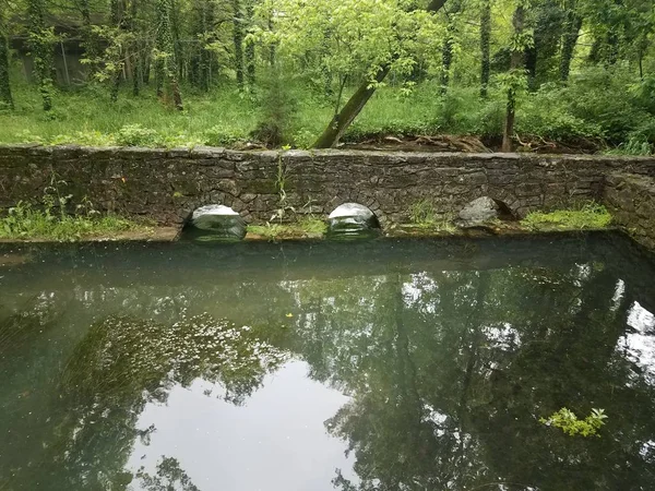 Muro di pietra con fori e acqua o fiume che scorre — Foto Stock