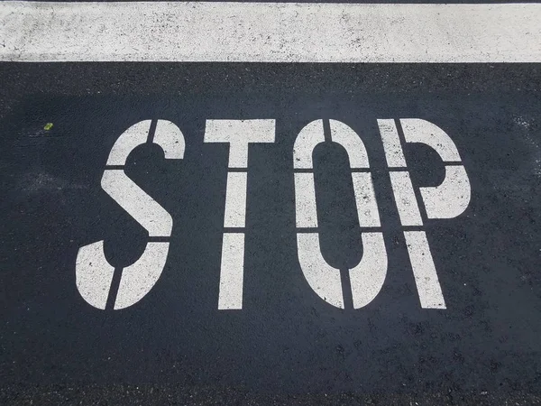Segnale di stop bianco dipinto su strada asfaltata nera — Foto Stock