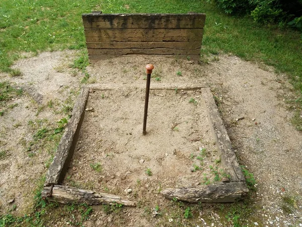 metal pole in horseshoe pit with wood backstop