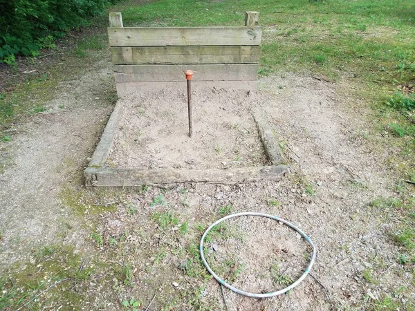 metal pole in horseshoe pit with wood backstop and plastic circle