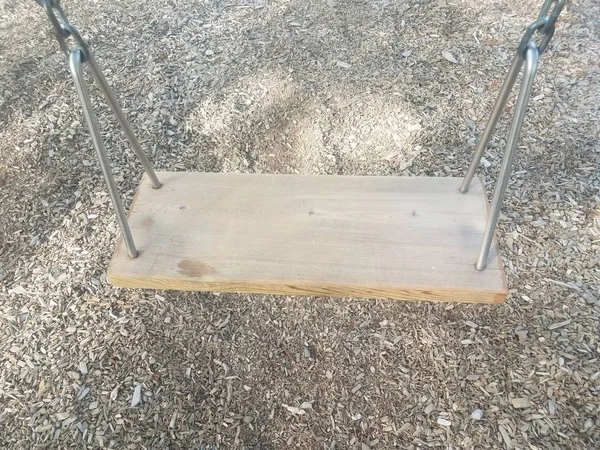 swingset with wooden seat on swing and mulch or wood chips