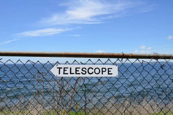 金属フェンスと海に白い望遠鏡の看板 — ストック写真