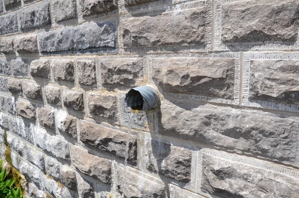 Acqua che esce dal tubo in muro di mattoni grigi — Foto Stock