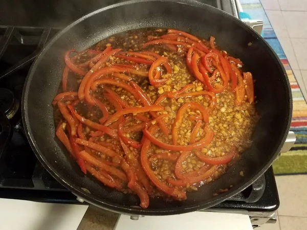 Red peppers and garlic cooking in frying pan — Stock Photo, Image