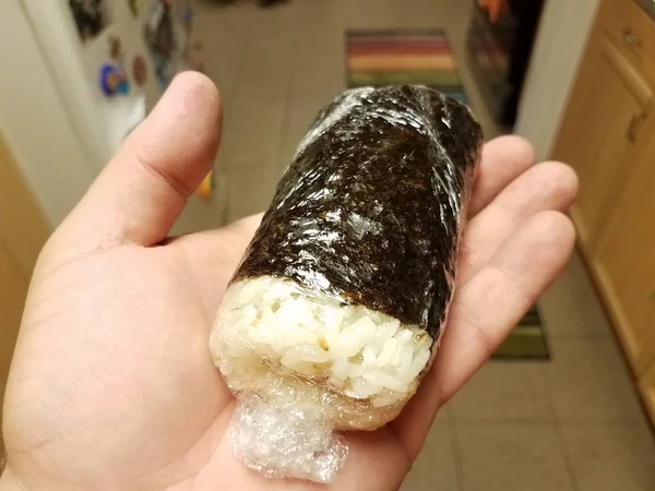 Mão segurando arroz embrulhado em algas e plástico na cozinha — Fotografia de Stock