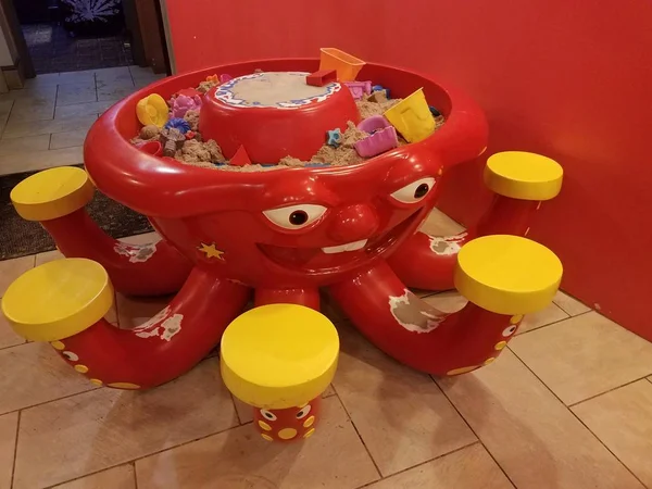 Пластиковый красный осьминог стол с песком и желтыми сиденьями — стоковое фото