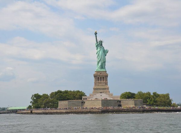 Statue of liberty on an island from the water with clouds