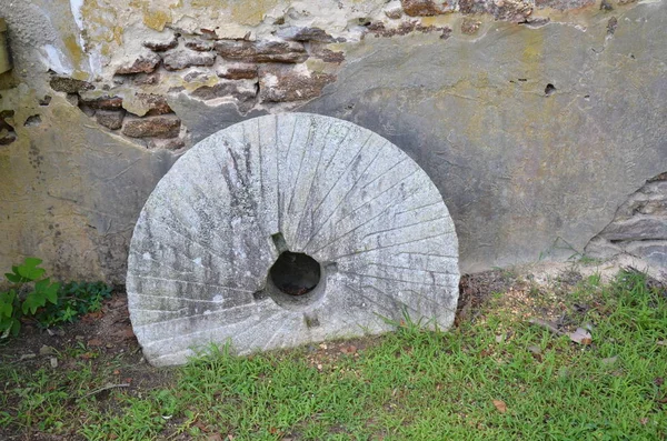 Круглий камінь з подрібнювача в землі біля старої цегляної стіни — стокове фото