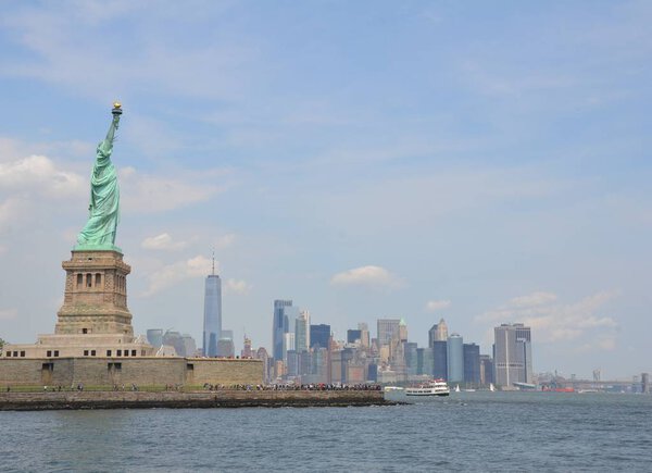 Copper statue of liberty in New York with buildings, water and ferries