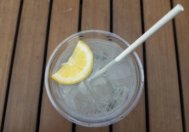 plastic cup with ice water and lemon and paper straw