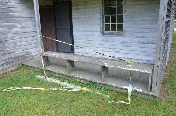 worn or weathered old wood house with yellow tape and do not enter sign on porch