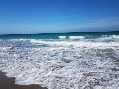 Sahilde ya da sahilde dalgalı ve mavi gökyüzü olan okyanus suyu