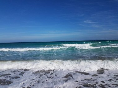 Sahilde ya da sahilde dalgalı ve mavi gökyüzü olan okyanus suyu
