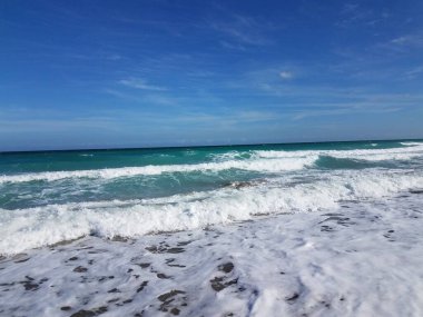 Sahilde ya da sahilde dalgalı ve mavi gökyüzü olan okyanus suyu