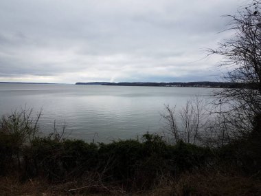 Göl veya gölet suyu ve bitki örtüsü ve bitkiler ve tepeler ve bulutlar