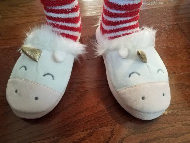 Ahşap zeminde kırmızı ve beyaz çizgili çoraplı beyaz ve pembe tek boynuzlu at terlikleri.