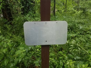 Ahşap direkte boş metal tabela ve arka planda bitkiler