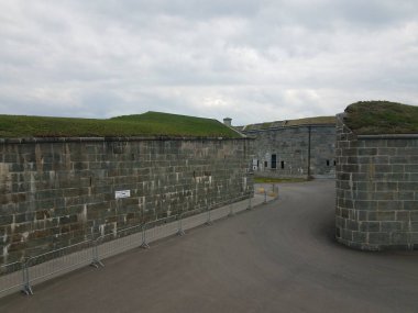Yol ve çimlerle kaplı gri kale duvarı ve İngilizce ve Fransızca giriş tabelası