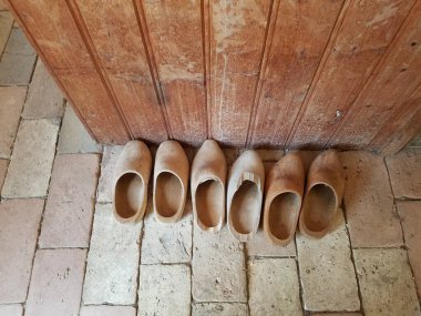 Ahşap bir duvarın yanında tuğla taş zeminde birkaç tahta ayakkabı.