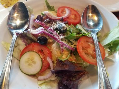 Salatalı, salatalı, domatesli ve kaşıklı beyaz bir kase.