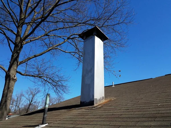 shingle roof with tall metal smokestack or chimney and tree
