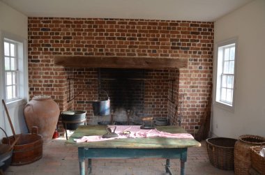 Kırmızı tuğlalı şömine, sepetler, masa ve eski metal demirler.