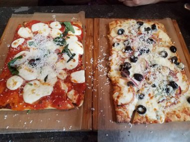 Domates, fesleğen, peynir ve tahtada siyah zeytinli pizza.