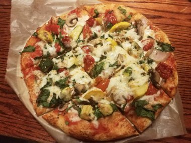 Tahta masa üzerinde peynirli ve balmumu kağıtlı sebze pizzası.