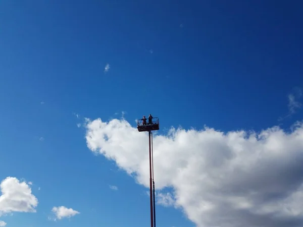 people at the top of a cherry picker or tower or lift and blue sky with cloud