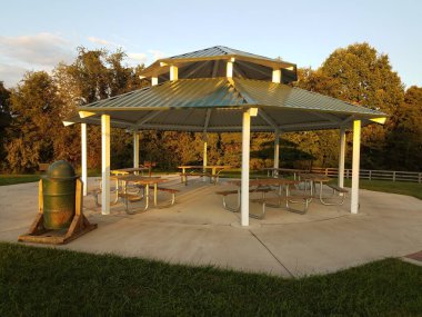 an outdoor pavillion with picnic tables, grill, and a trash can clipart