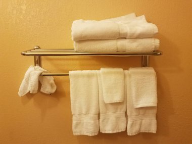 turuncu banyo duvarı ve metal raflarda beyaz havlular.
