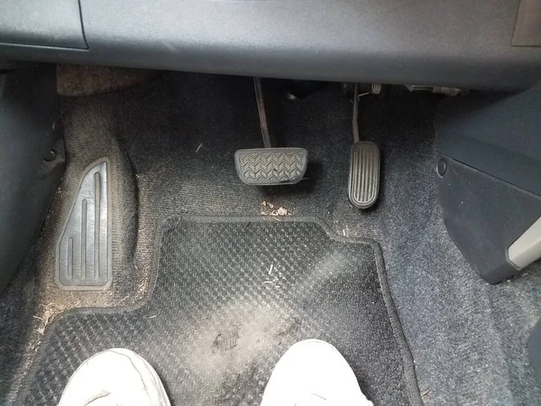 view of the gas and brake pedals in a dirty car