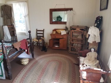 Beşiği, bebeği, lazımlığı, sandalyeleri ve penceresi olan eski ahşap yatak