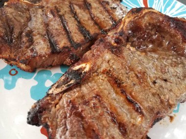 İki sulu ızgara biftek, beyaz ve mavi tabakta.