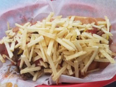 Biftek, soğan ve patates kızartmasıyla kaplı sepetteki sosisli sandviç.