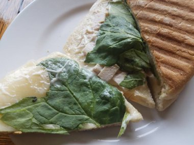 Tahta bir masada peynirli, jambonlu ve ıspanaklı ızgara sandviç.