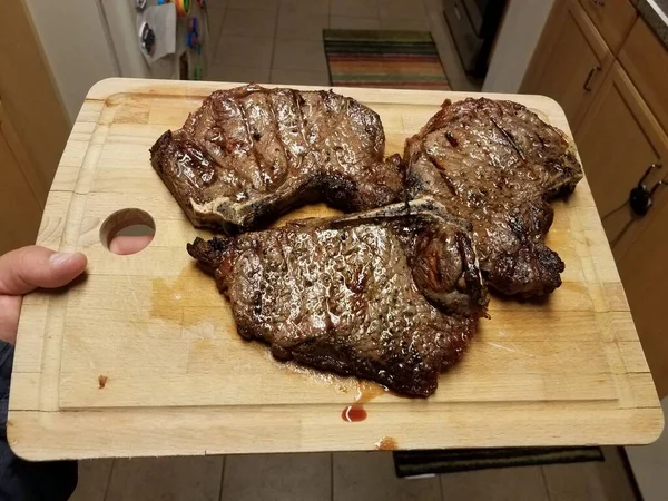 Mão Segurando Placa Corte Madeira Com Bifes Carne Grelhados Cozinha — Fotografia de Stock