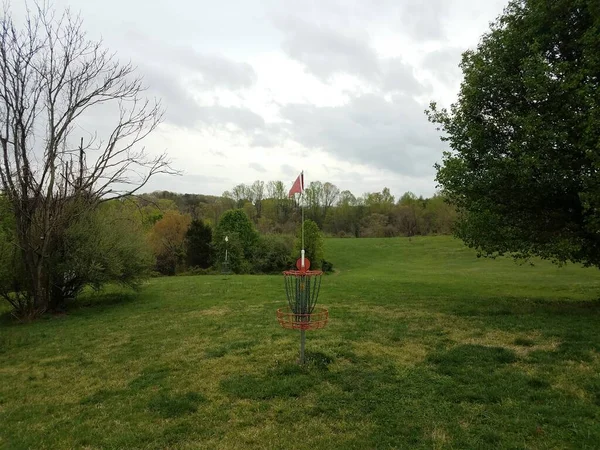 red disc golf chain basket or hole with green grass and trees