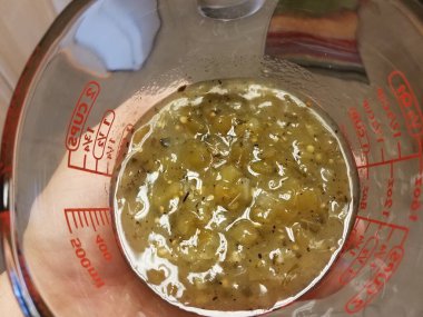 Baharatlı yeşil salsa sosuyla ölçü kabı tutan el.