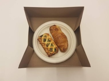 Bir ıspanak ve kahverengi bir kutuda beyaz bir tabakta başka bir kruvasan.