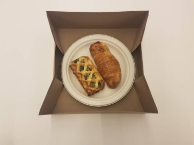 Bir ıspanak ve kahverengi bir kutuda beyaz bir tabakta başka bir kruvasan.