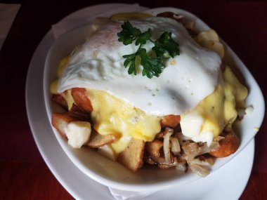 Beyaz tabakta patates, yumurta ve sarı sos.